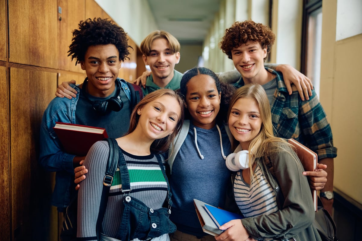 Multiracial group of happy classmates at a high school hallway looking at camera