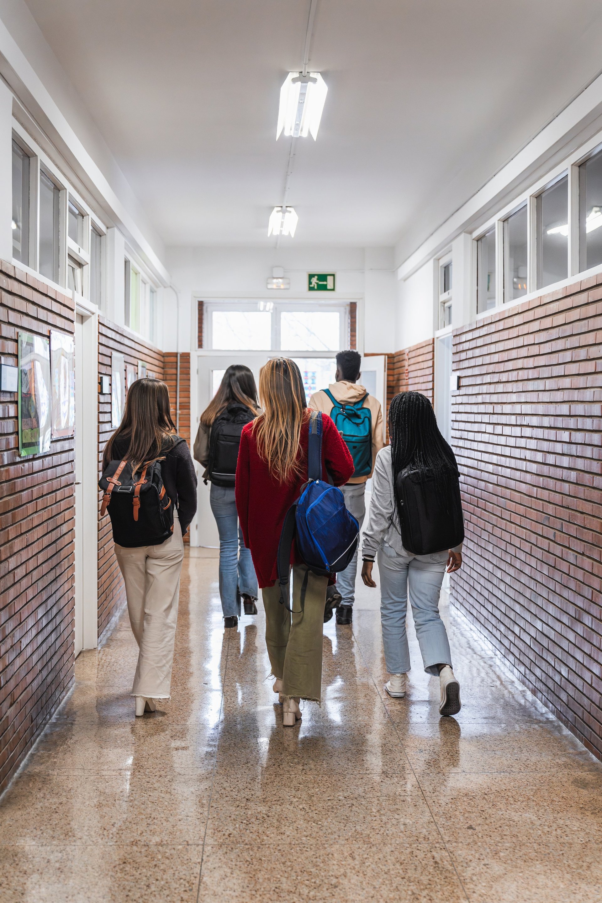Five American high school students walking together down a busy school hallway with backpacks