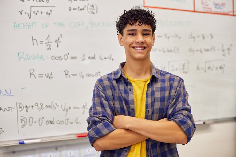 Confident teenage student smiling with arms crossed in front of a whiteboard after solving a problem