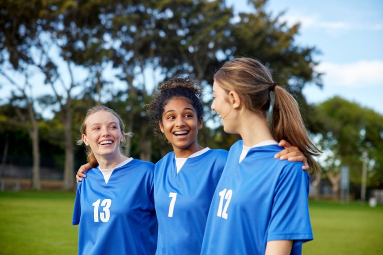 Three smiling teenage girls in sports uniform walking together on a grassy field after a game