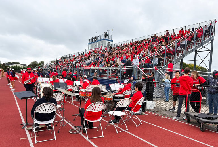 Cheerful fans in the stands and a lively band performing at an American high school football game