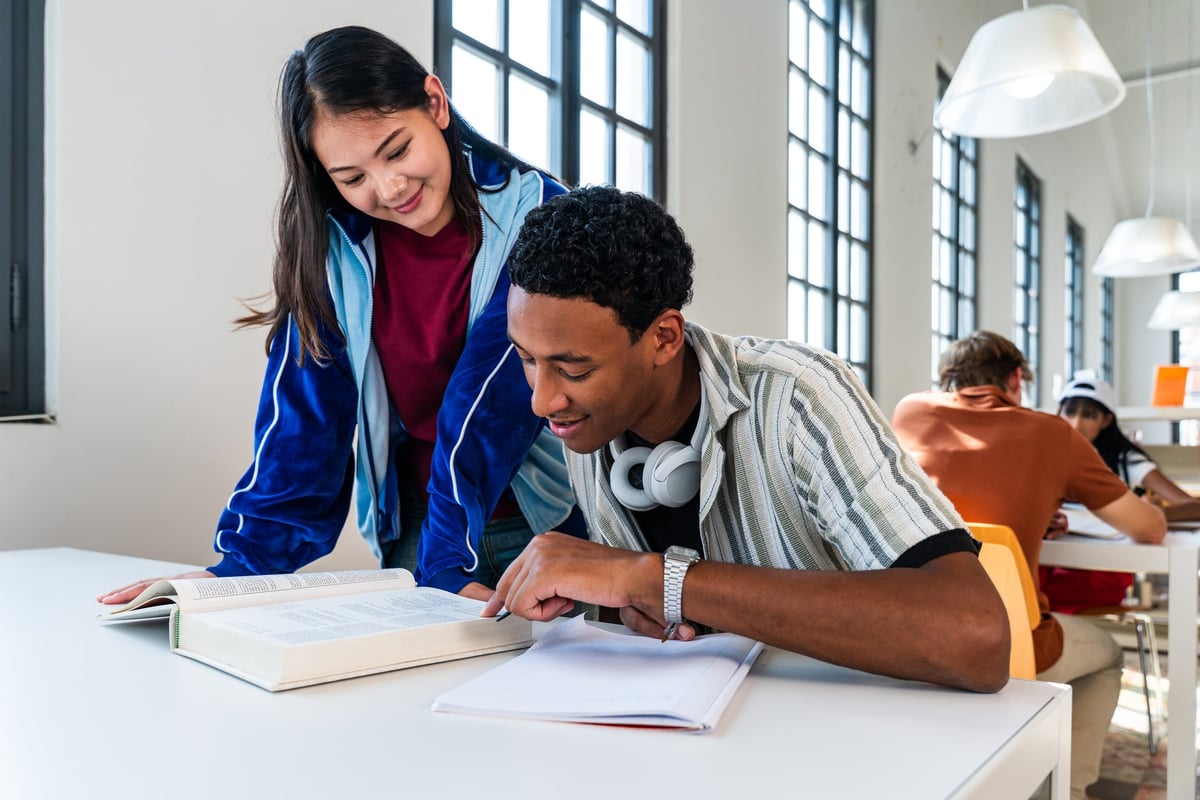 Multiethnic group of young students meeting at the library - multiethnic young students working together on a project, studying a book and taking notes in a modern university library