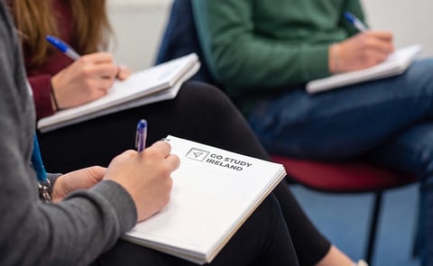 Three people sitting in a circle holding notepads and pens during a group discussion or meeting