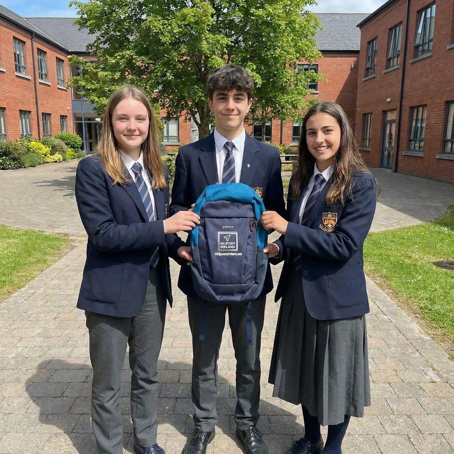 Three students in school uniforms holding a blue backpack in a courtyard with brick buildings behind them