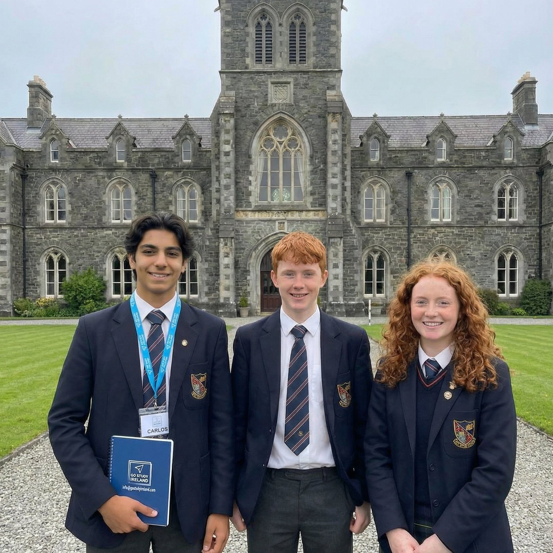 Three students in school uniforms stand in front of a large stone Gothic building with a central tower