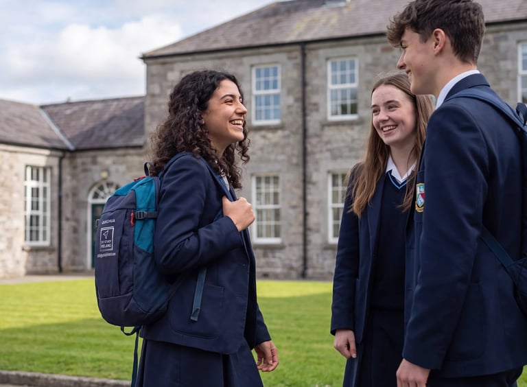Three students in school uniforms standing together on a lawn in front of a stone building, smiling and conversing