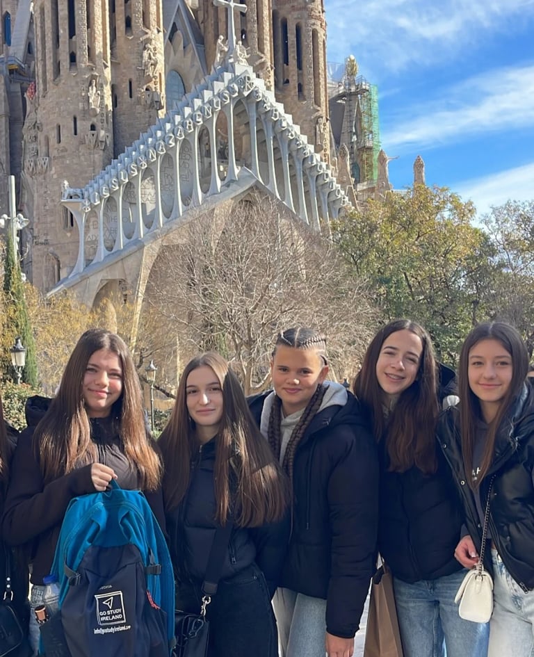 Five young women posing together in front of a Gothic cathedral with blue sky in background