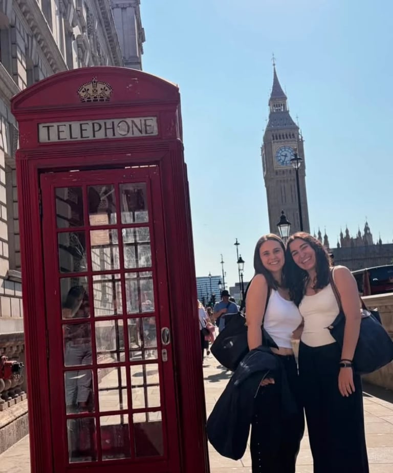 Two women posing together next to a red British telephone booth with Big Ben visible in the background in London