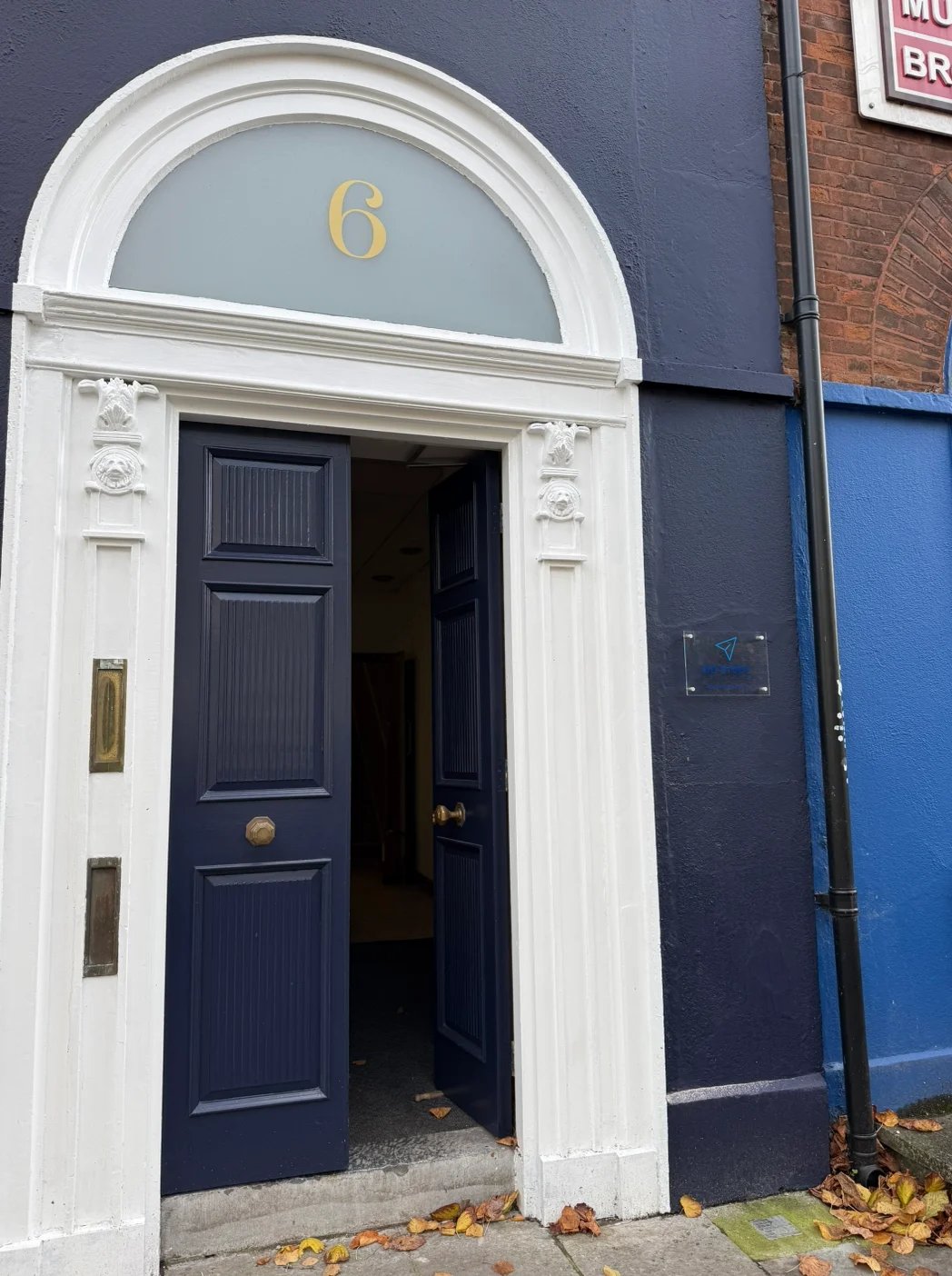Traditional townhouse entrance with dark blue door number 6, white trim, and arched fanlight above the doorway on a city street