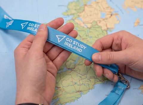 Hands holding a blue Go Study Ireland lanyard against a map of Ireland in the background