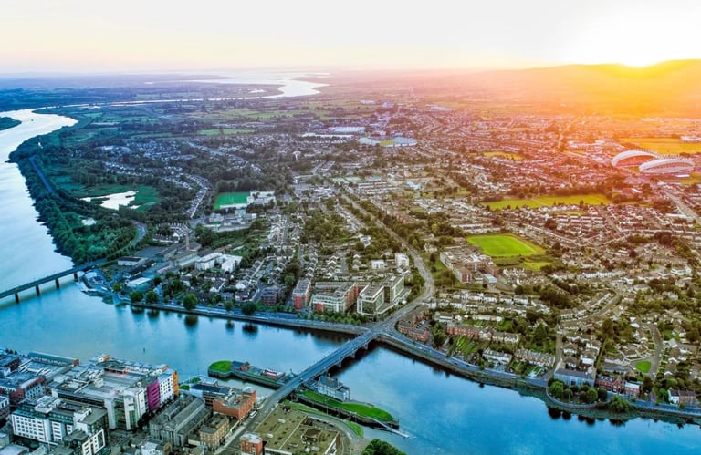Aerial view of a sprawling river-side city at sunset with bridges, neighborhoods, and waterways visible below